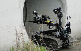 a tactical robot with tracks enters an underground concrete pipe carrying an array of sensors and cameras.