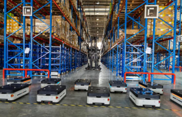 Ten autonomous mobile robot lined up on the floor in a warehouse setting.