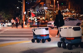 Two Cartken delivery robots crossing a street at night.