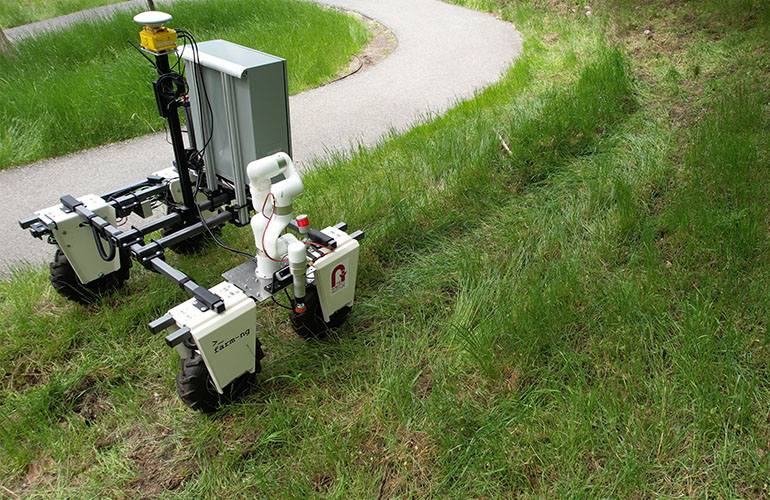A wide view of the TartanPest robot in a field near a sidewalk. 