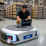 an engineer updates software on a Geek+ mobile robot with a laptop in the middle of a warehouse.